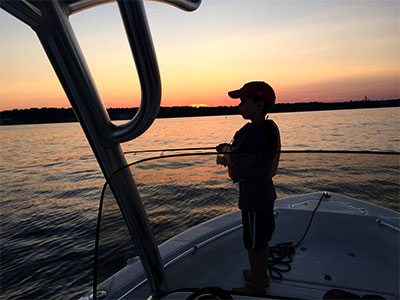 boy fishing on the bow of a boat at sunset